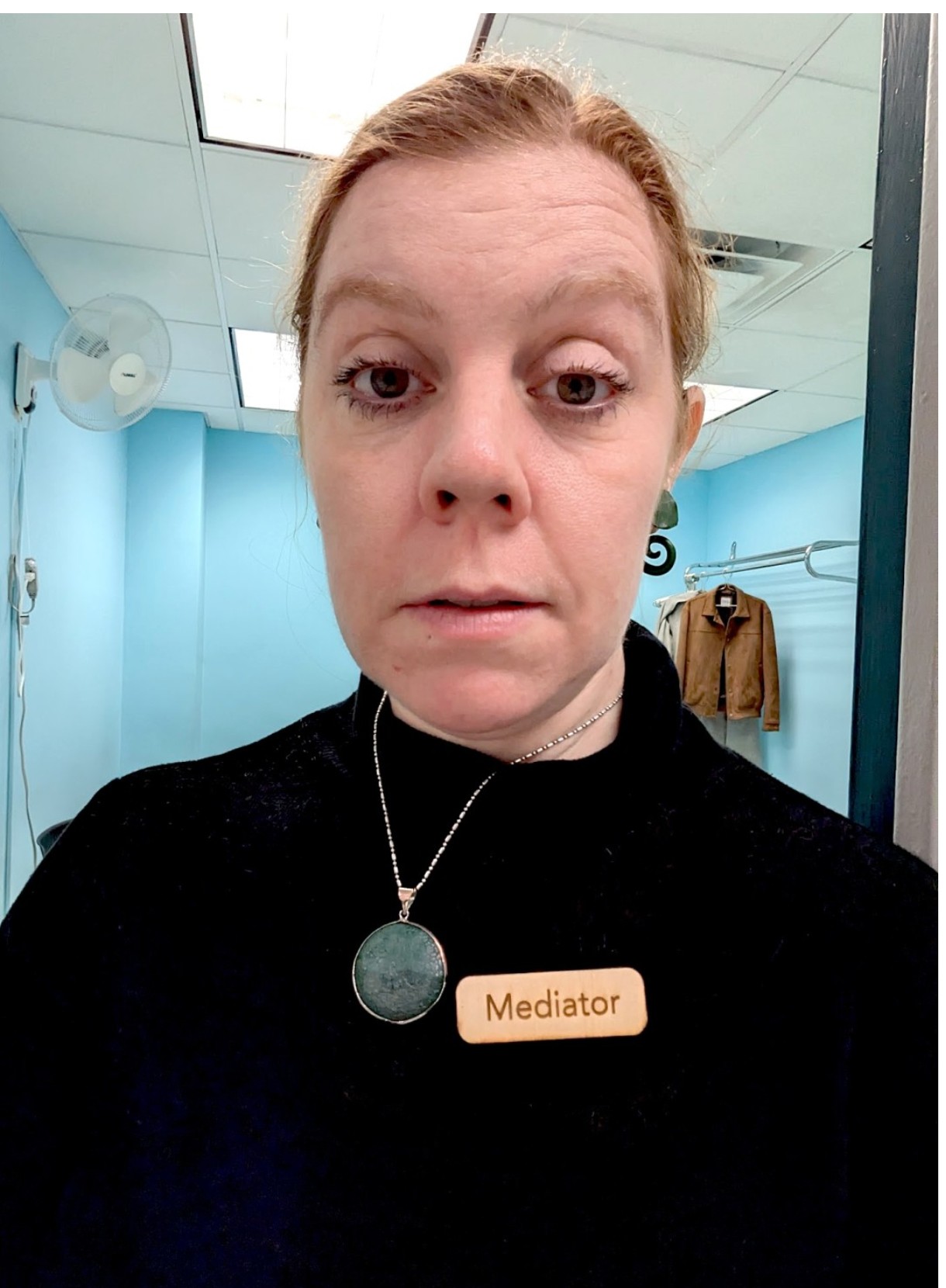 Ida Benedetto wearing a wooden Mediator name badge in a small claims court waiting room.